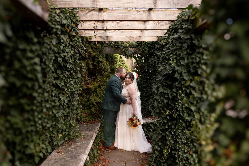 A romantic wedding moment captured in a garden pathway lined with lush ivy-covered walls.