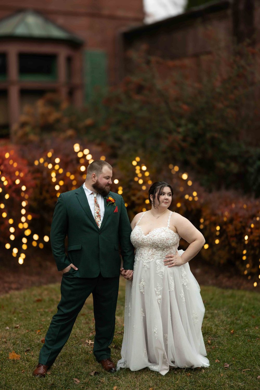 Wedding couple poses in front of decorative string lights at an outdoor autumn venue.