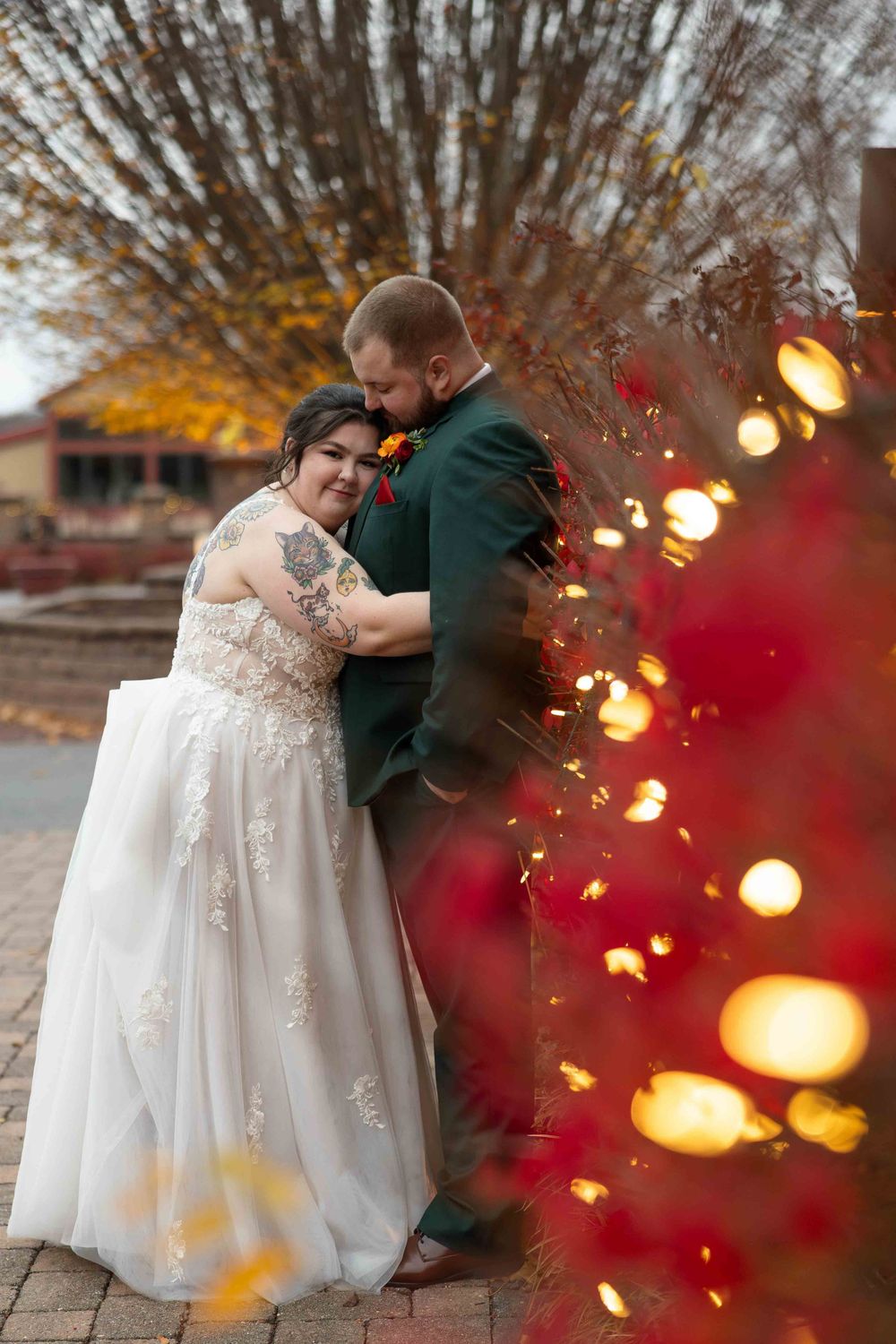 A romantic winter wedding photo with a couple embracing near illuminated holiday lights at dusk.