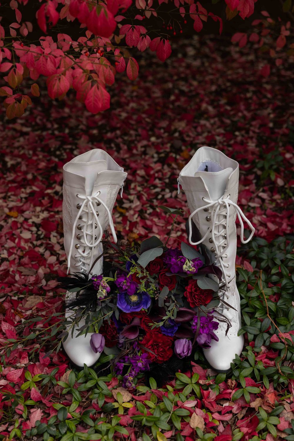 White vintage lace-up boots adorned with purple and blue flowers against a backdrop of vibrant red autumn leaves.