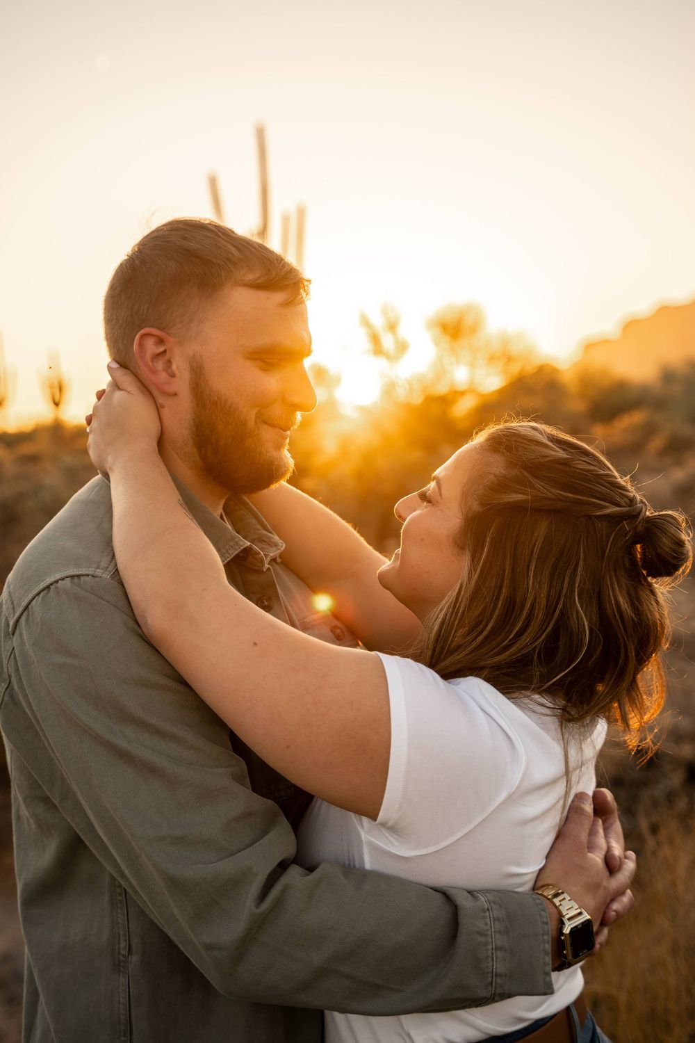 A romantic desert sunset silhouettes a couple embracing against a golden sky with saguaro cacti.