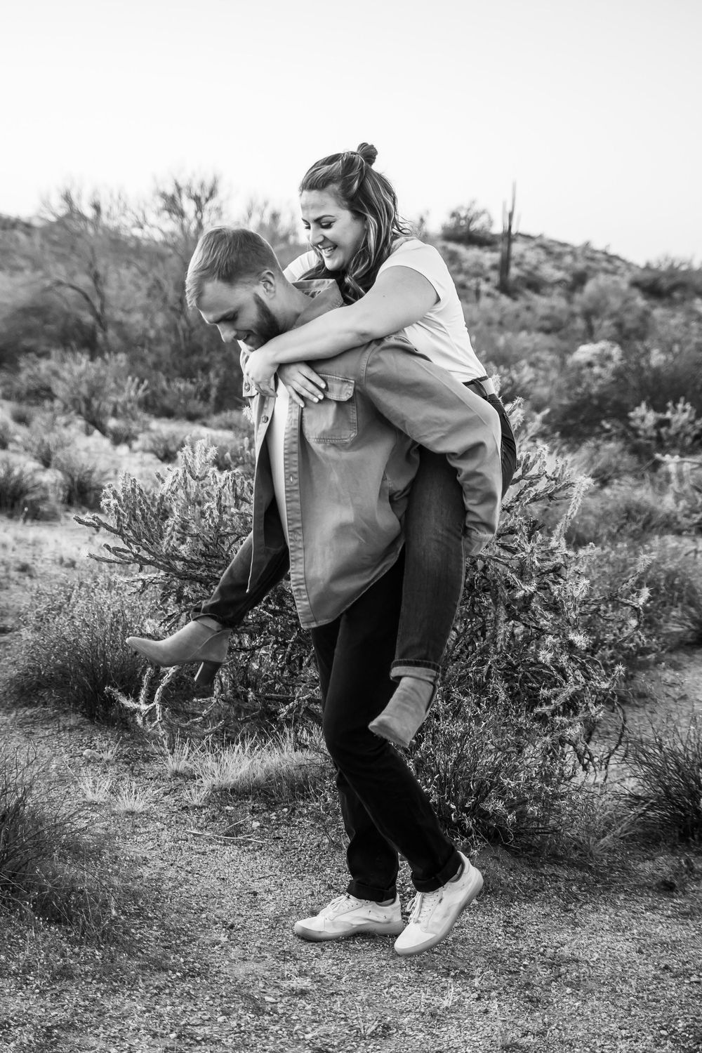 Black and white photos capture playful moments of a couple dancing and embracing in a desert landscape.