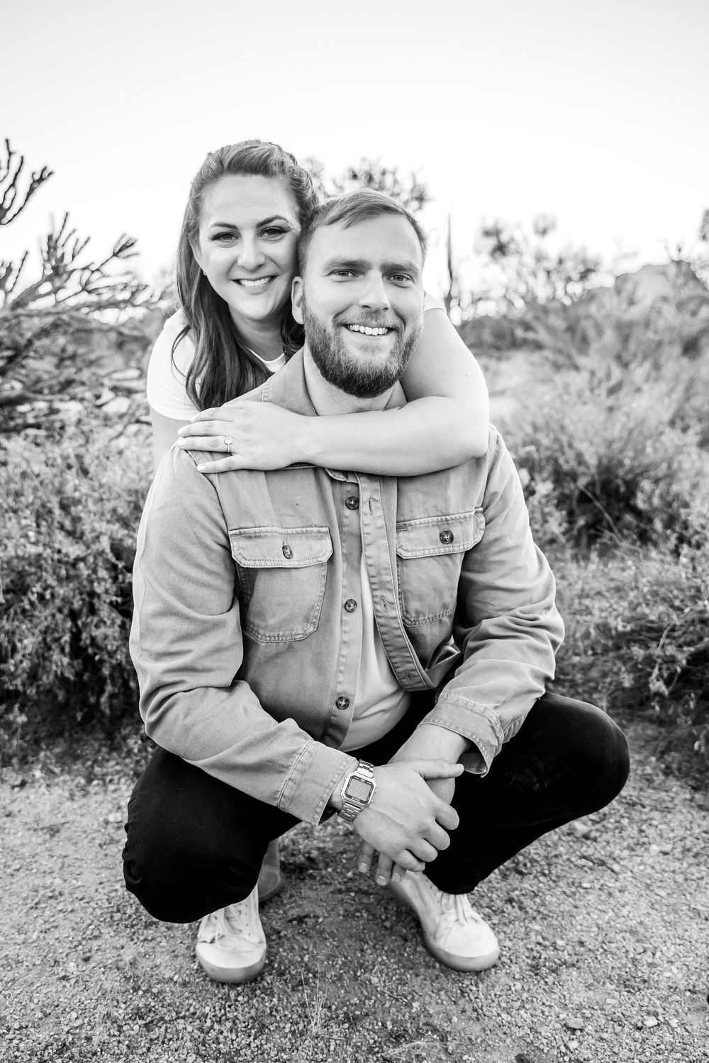 Black and white portraits of couple in denim jackets sitting together on desert ground.