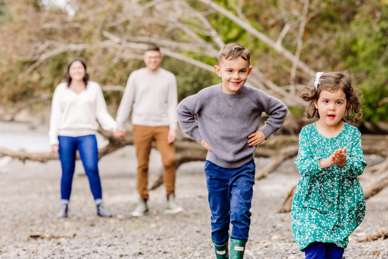 Two children run and play on a beach path while their parents hold hands in the background.