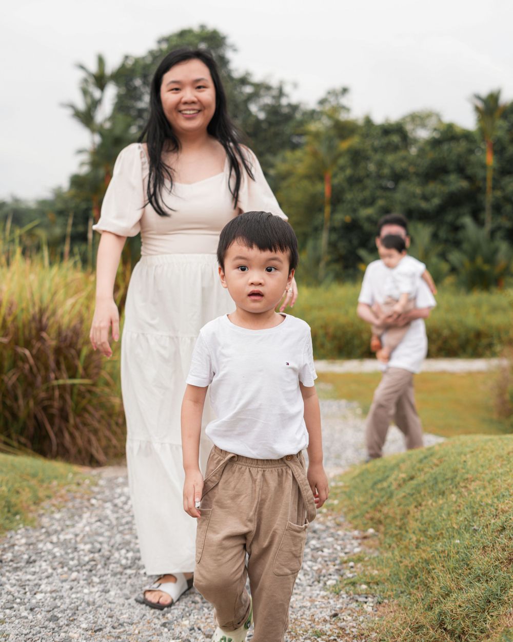 A parent and child walking along a gravel path with tall grass in the background.