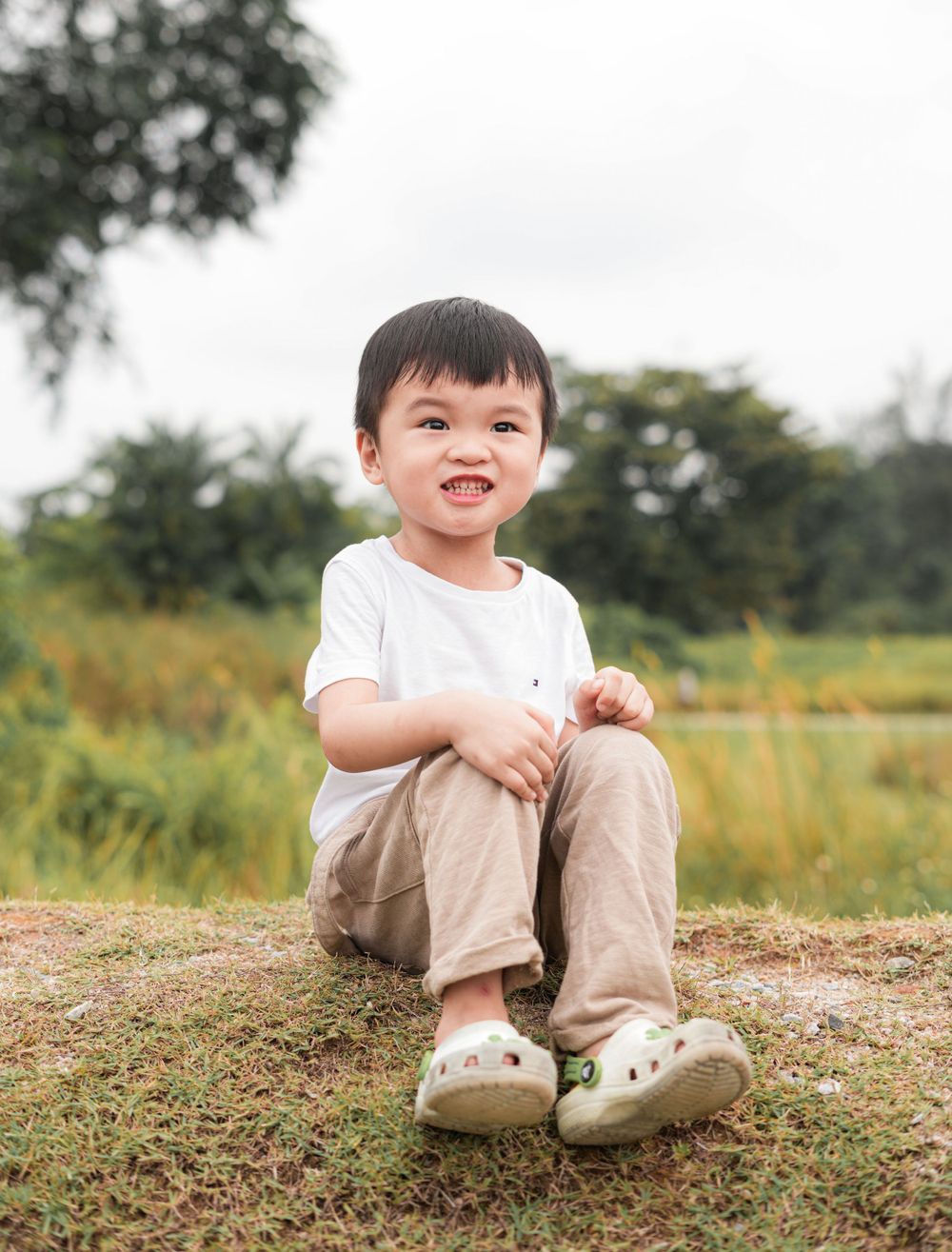 A child in casual attire sits on a small hill overlooking a natural landscape.