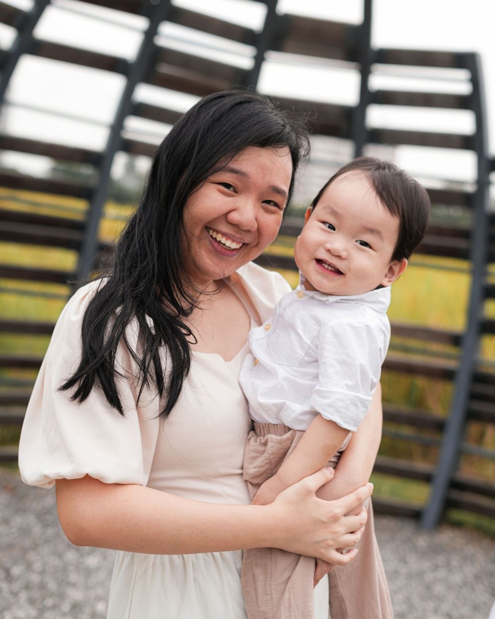 A joyful mother and baby share a candid moment together against a wooden structure backdrop.