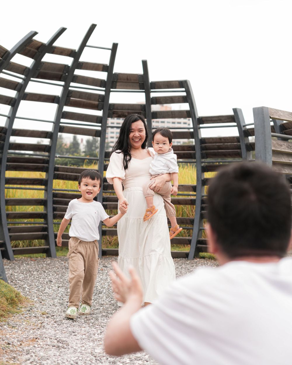 A family poses playfully in front of a wooden art installation on a gravel path.