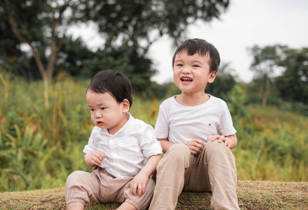 Two young children in white shirts sit together outdoors sharing a laugh.