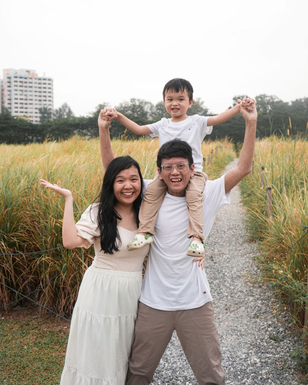A happy family poses playfully on a gravel path surrounded by tall grass.