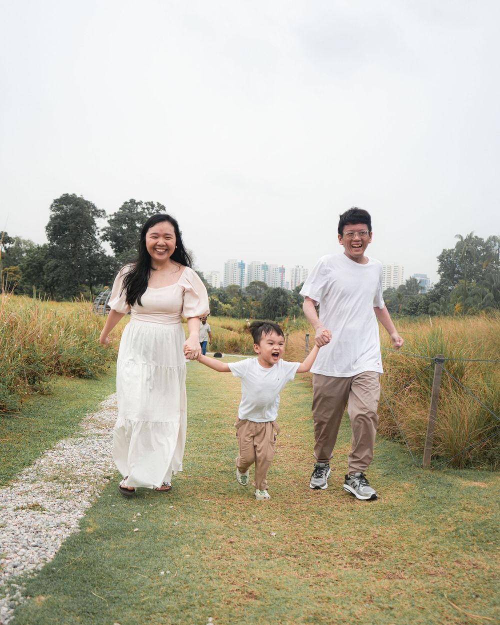 A family runs joyfully together on a gravel path through a scenic outdoor area.
