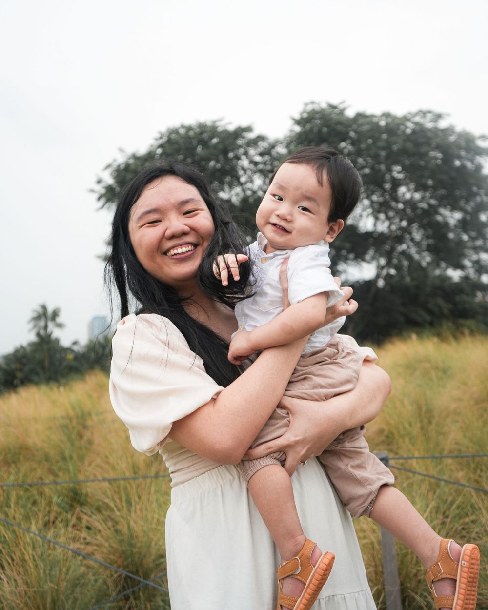 A mother and child share laughter while posing together in an outdoor setting.