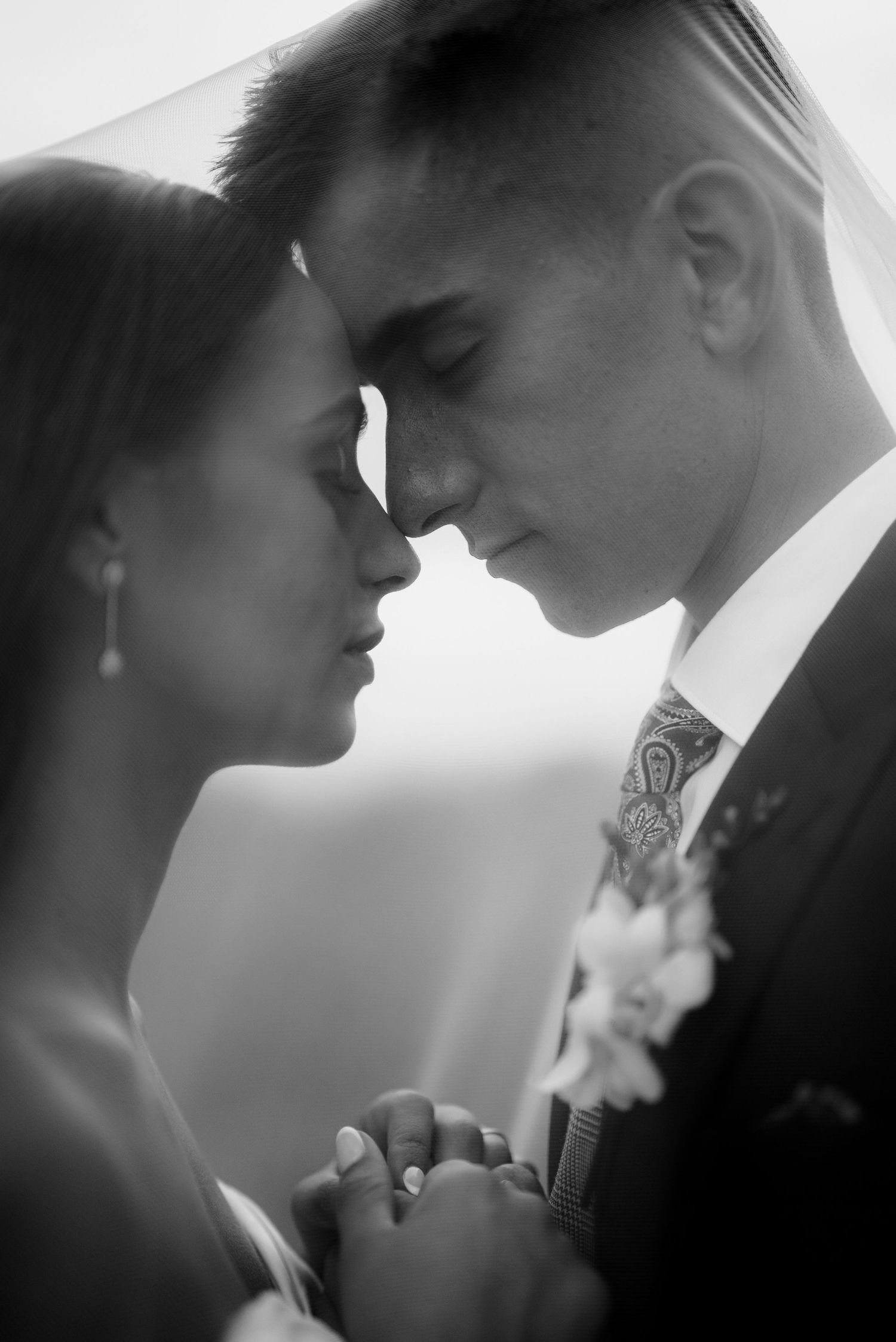 Intimate black and white wedding portrait of couple in formal attire sharing a romantic moment with foreheads touching.