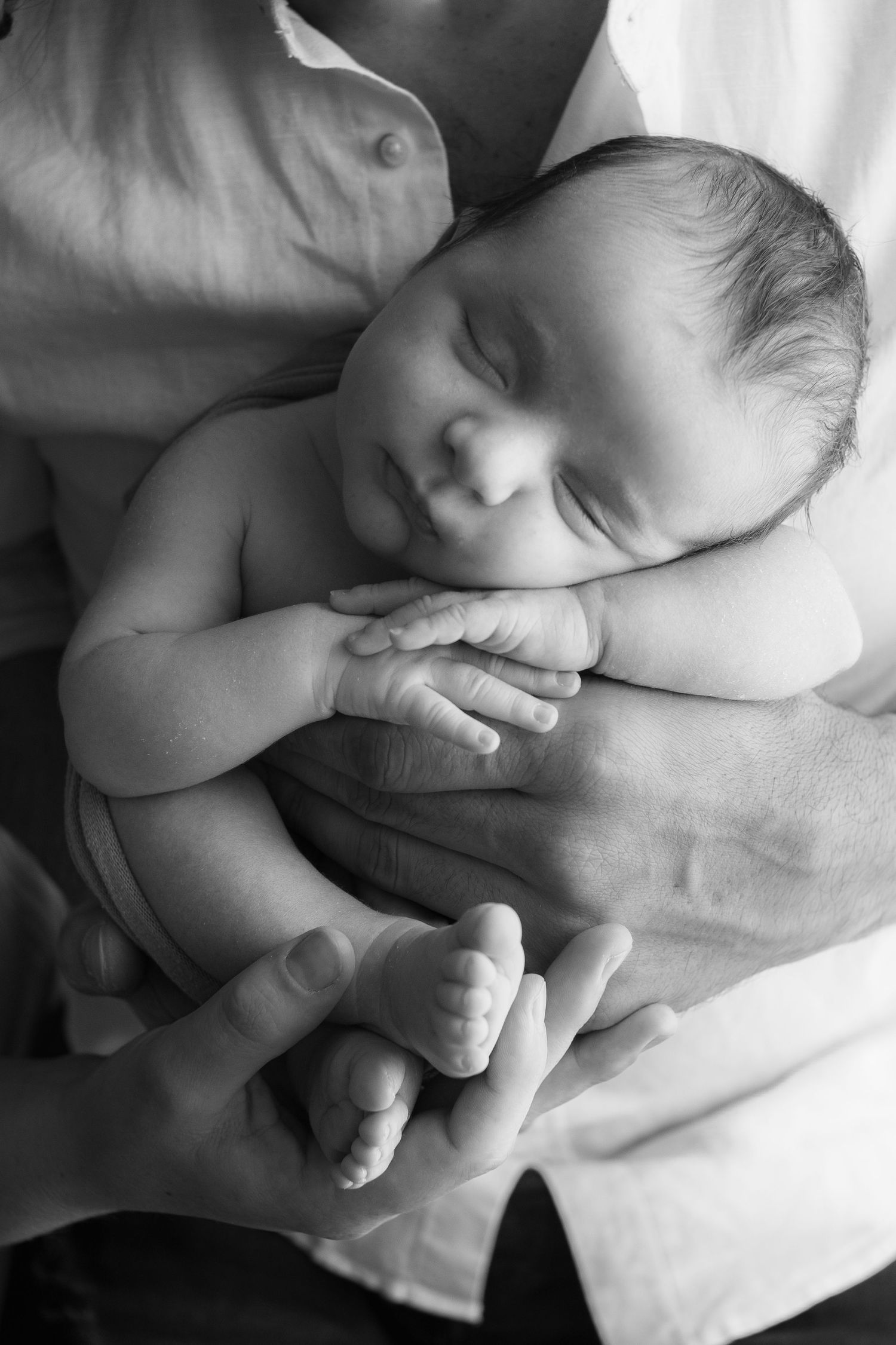 Un neonato che dorme pacificamente cullato in mani gentili del papà in bianco e nero.