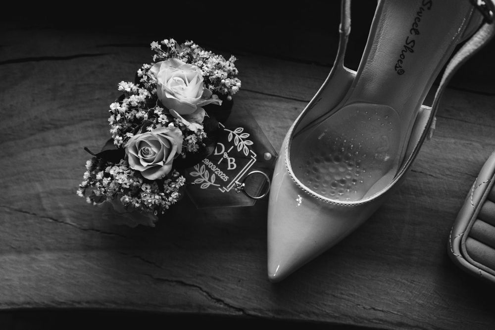 Accessori da sposa tra cui tacchi argentati e delicate composizioni floreali disposte su una superficie scura. fotografia artistica in b&w.