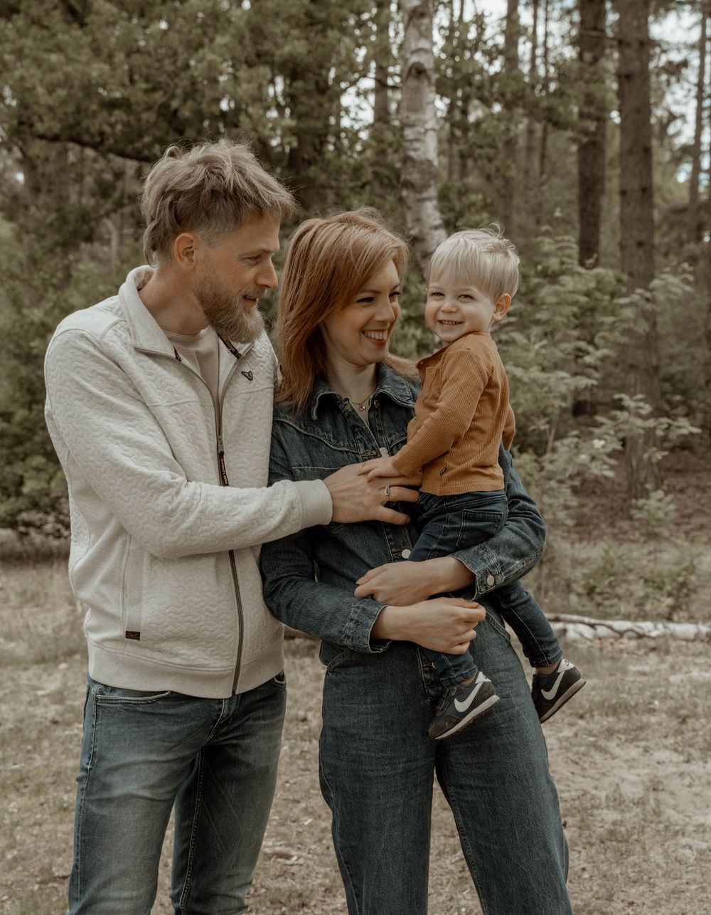 Family sharing tender moments together outdoors in casual denim and earth-toned clothing.
