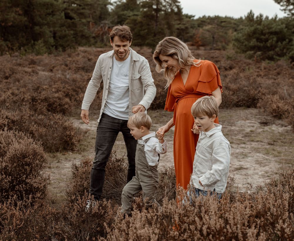A family in earth-toned clothing walks together through a rustic outdoor setting during golden hour.