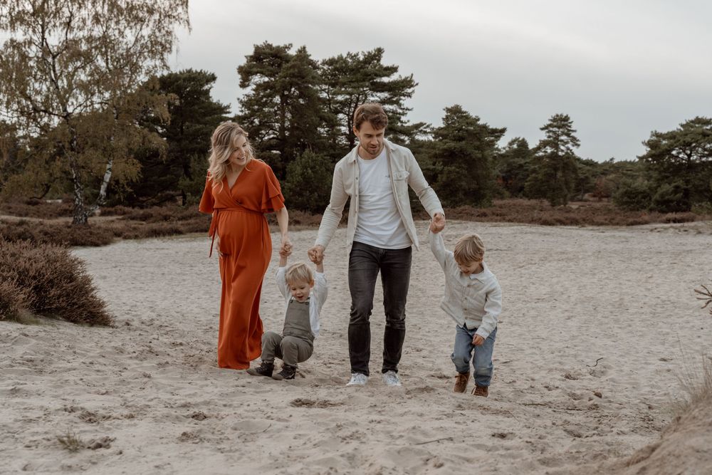 A family walks together along a scenic beach path during sunset with pine trees in the background.