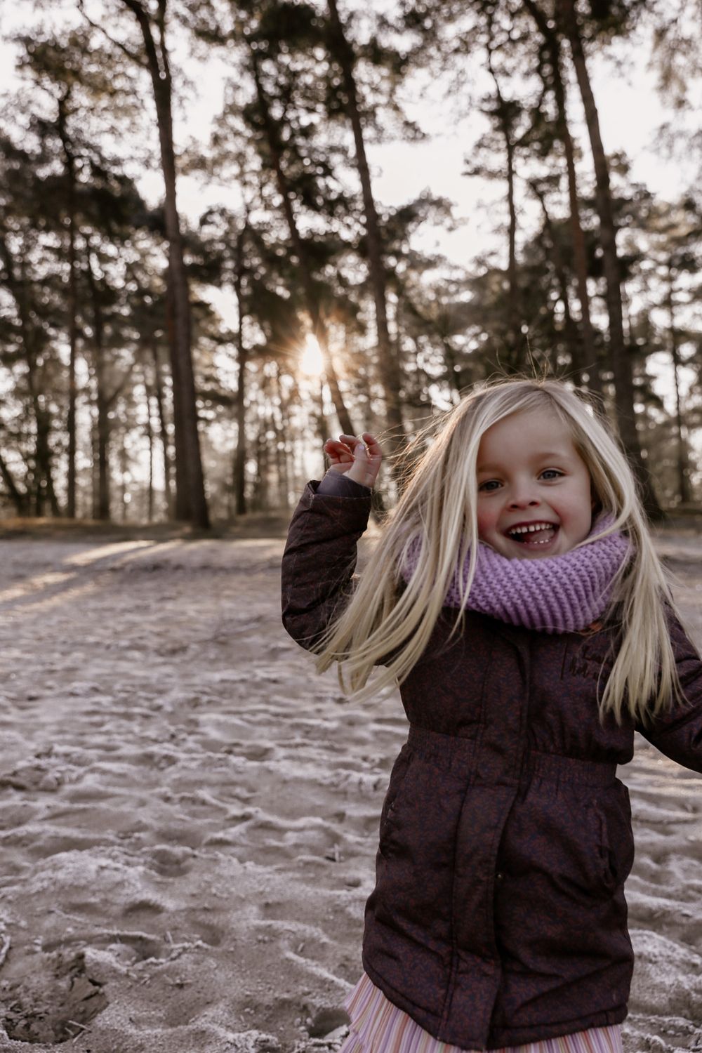 Winter scene of someone playing joyfully in the snow among pine trees at sunset.