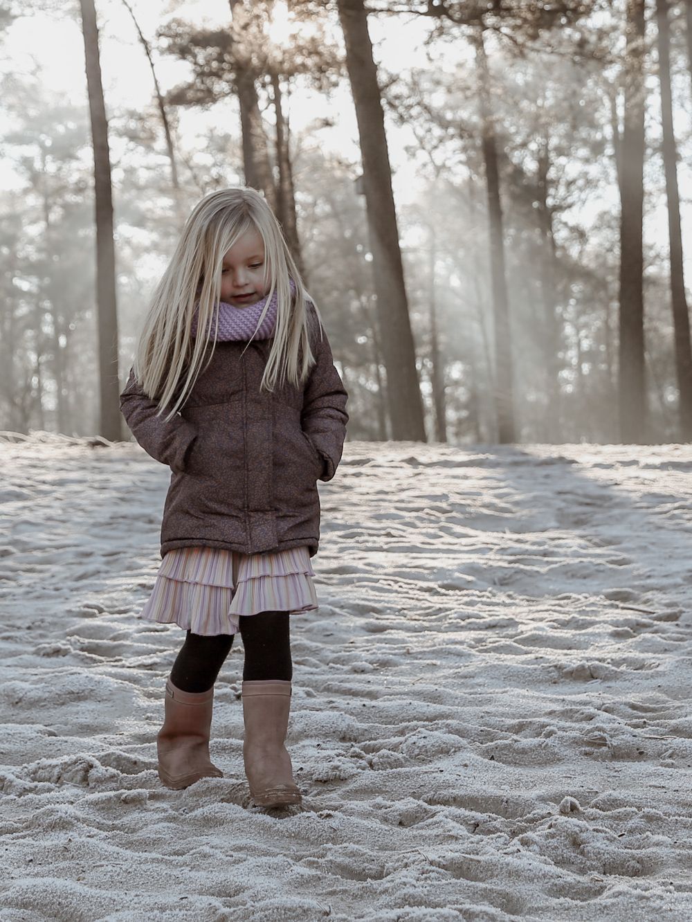 Person in winter clothing exploring snowy forest ground during golden hour.