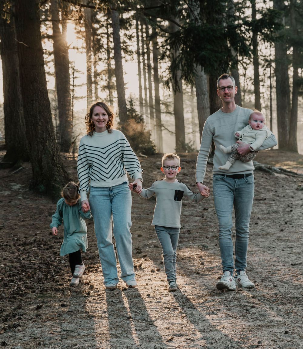 Family walking through sunlit forest path during golden hour photo session.