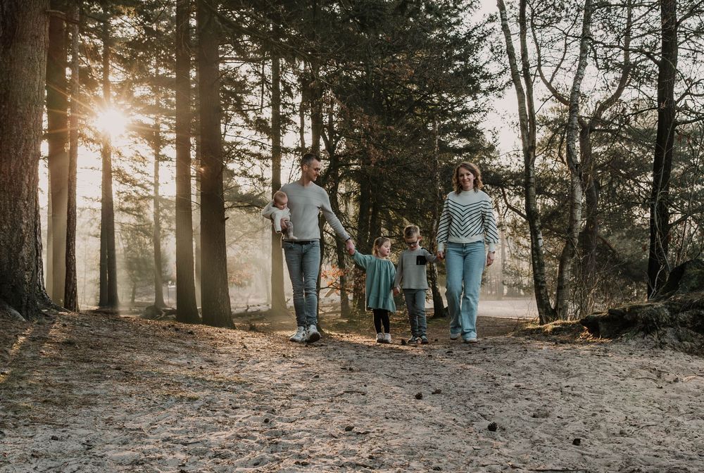 Silhouetted family figures walking along wooded trail at sunset.
