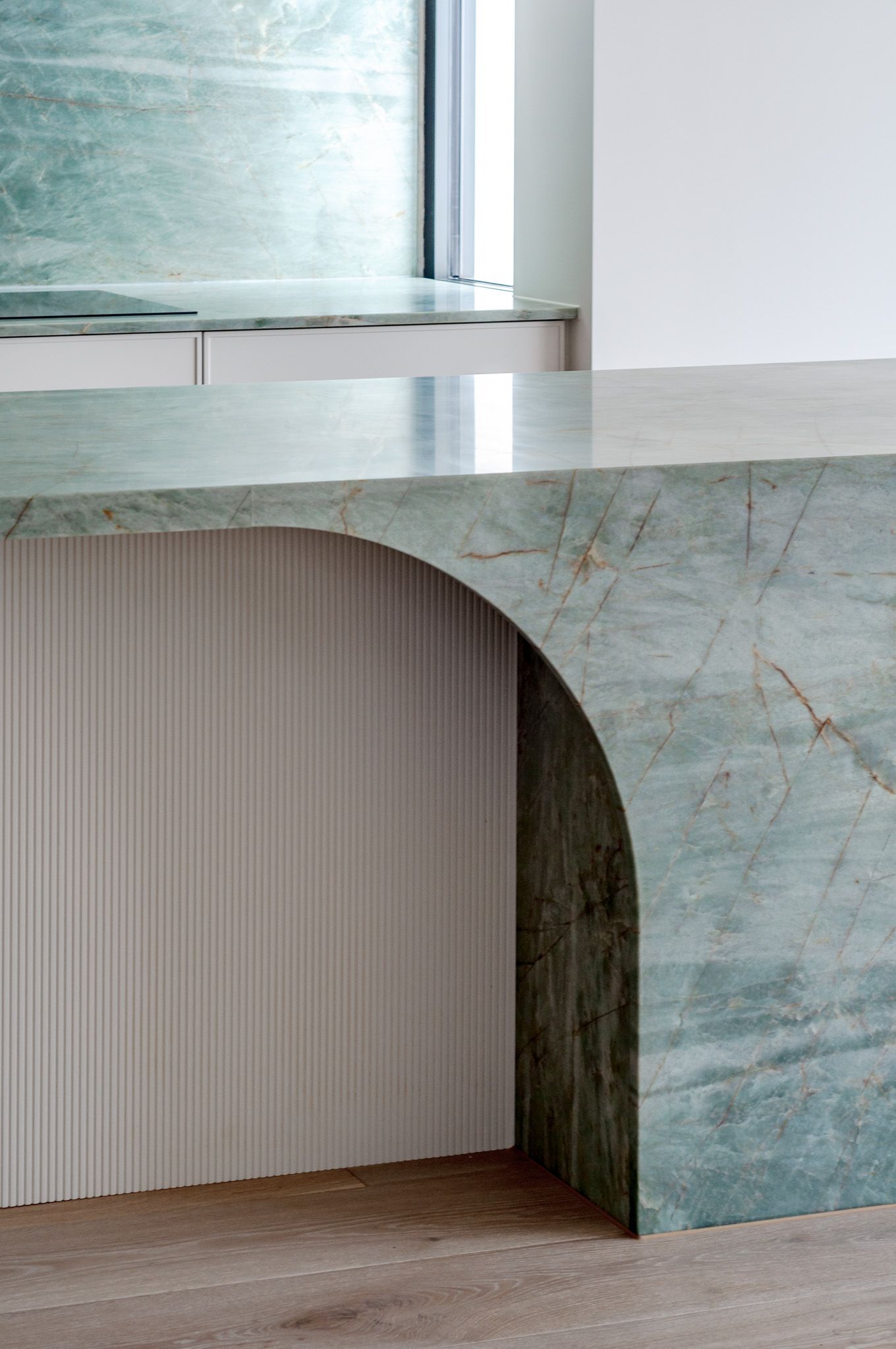 Modern interior design featuring a curved marble countertop in soft blue tones with a ribbed panel underneath.