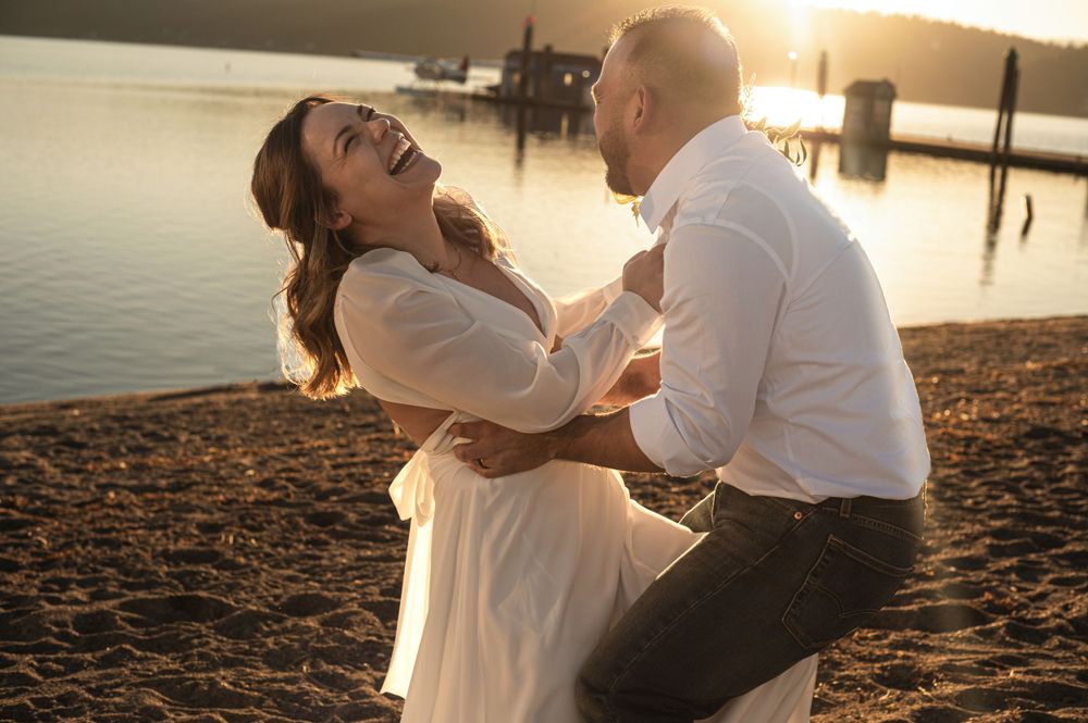 A newly married couple playing on a beach in a portrait in CDA Idaho. Taken by Jessica Rae Photography.