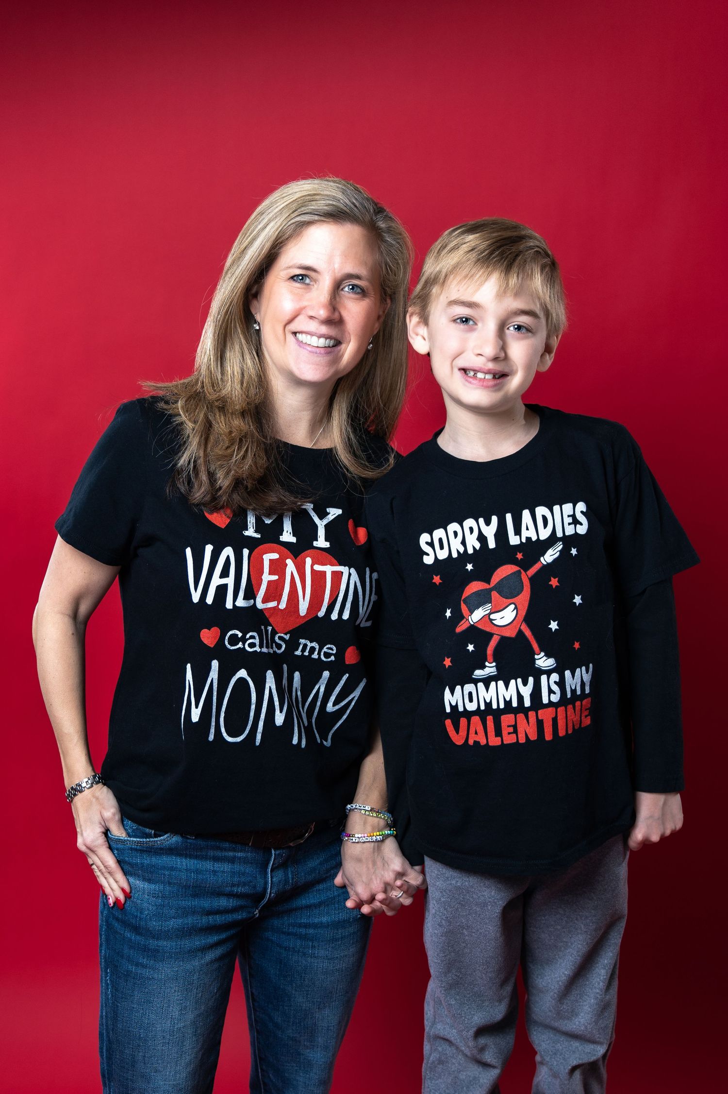 Parent and child wearing matching Valentine's Day themed black t-shirts against a red background.
