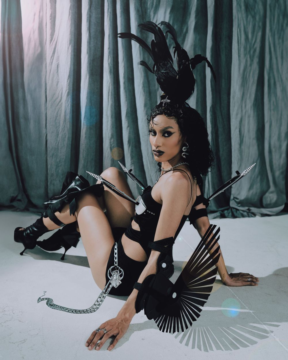 Dark theatrical fashion photo with dramatic black feather headpiece and fan accessories.