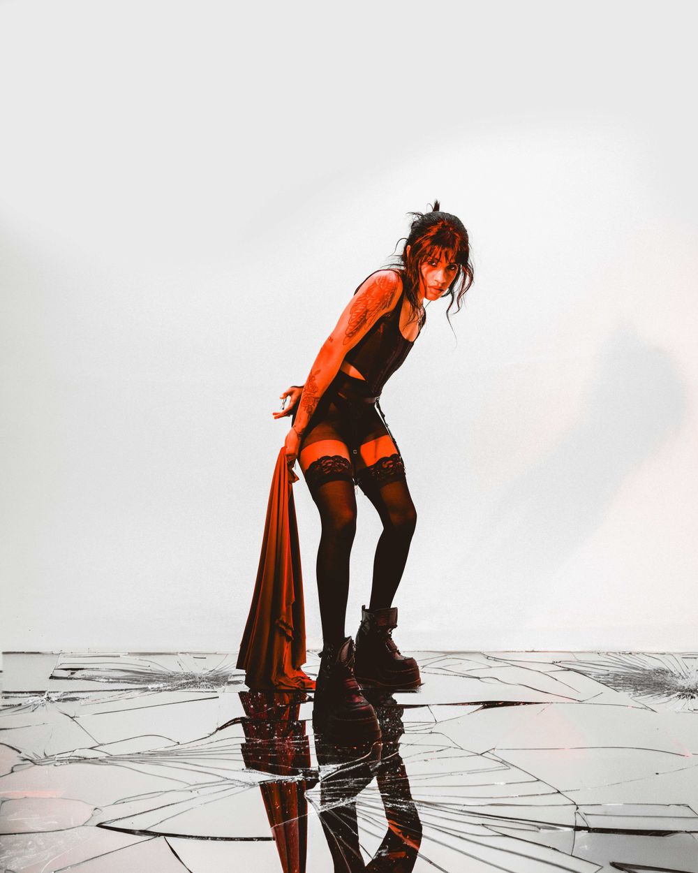 Dramatic fashion photo with model in orange coat and black boots against reflective surface.