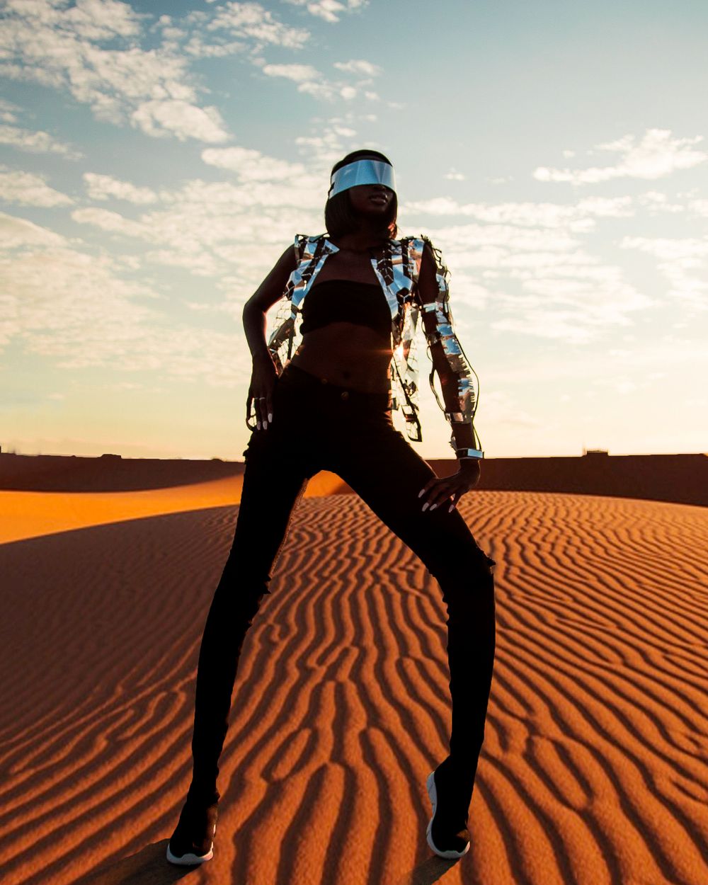 Silhouette poses dramatically on sand dunes against sunset sky.