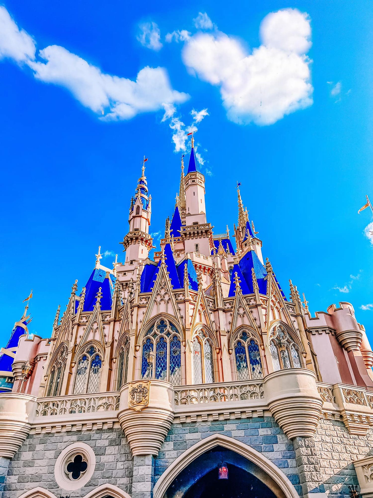 Cinderella Castle at Disney World features ornate blue and gold spires against a bright blue sky with white fluffy clouds.