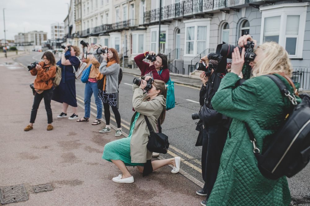 Line of photographers with cameras positioned along a coastal walkway.