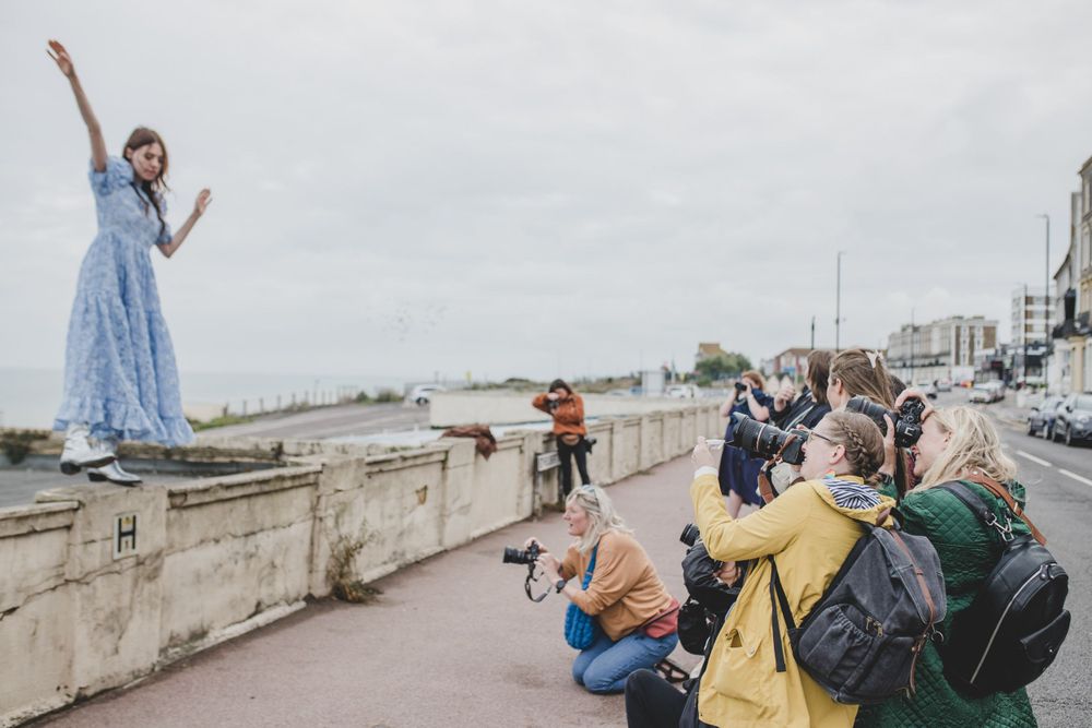 Photographers capturing shots of someone posing on a seaside wall.