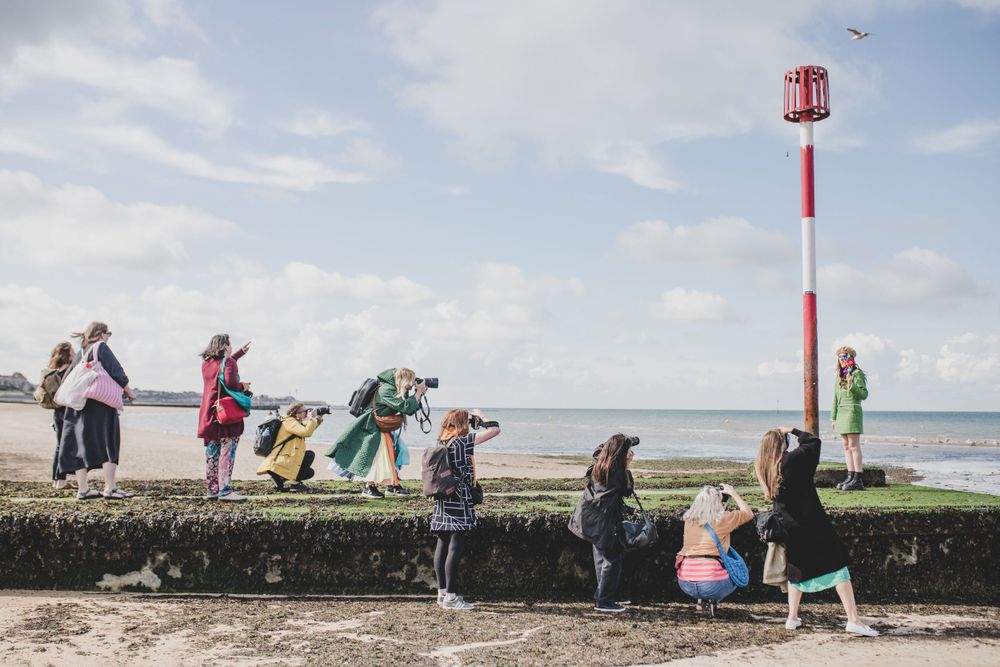 Photographers lined up along a seaside wall taking pictures against a cloudy sky.