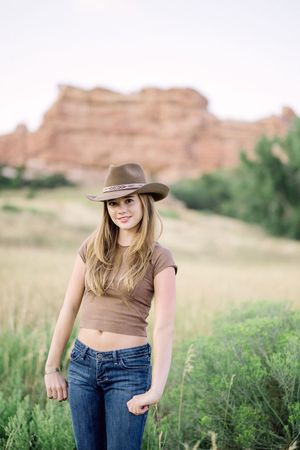 Casual western fashion photography against desert landscape with red rocks and green vegetation.