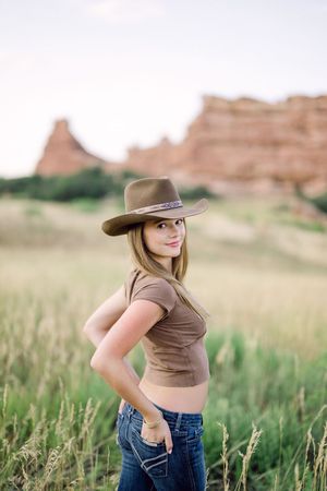 Western-style portrait in a field with red rock formations and tall grass in the background.