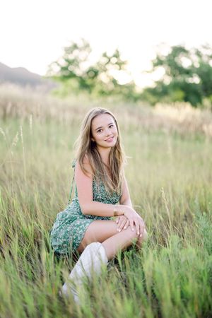 A green floral dress stands out against tall grass in a summer field during golden hour.