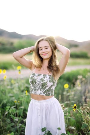 A dreamy summer portrait in a sunflower field with a white dress and floral crop top against rolling hills.