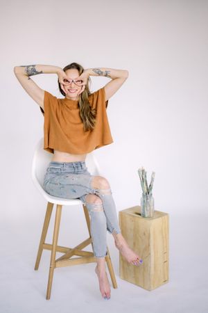 Casual portrait on wooden stool wearing orange crop top and distressed jeans.