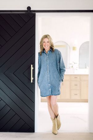 Denim shirt dress paired with tan cowboy boots standing in doorway with modern black barn door.