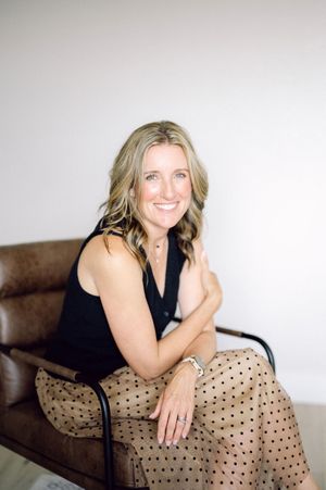 A person wearing a black sleeveless top and polka dot skirt sits casually on a brown leather chair.