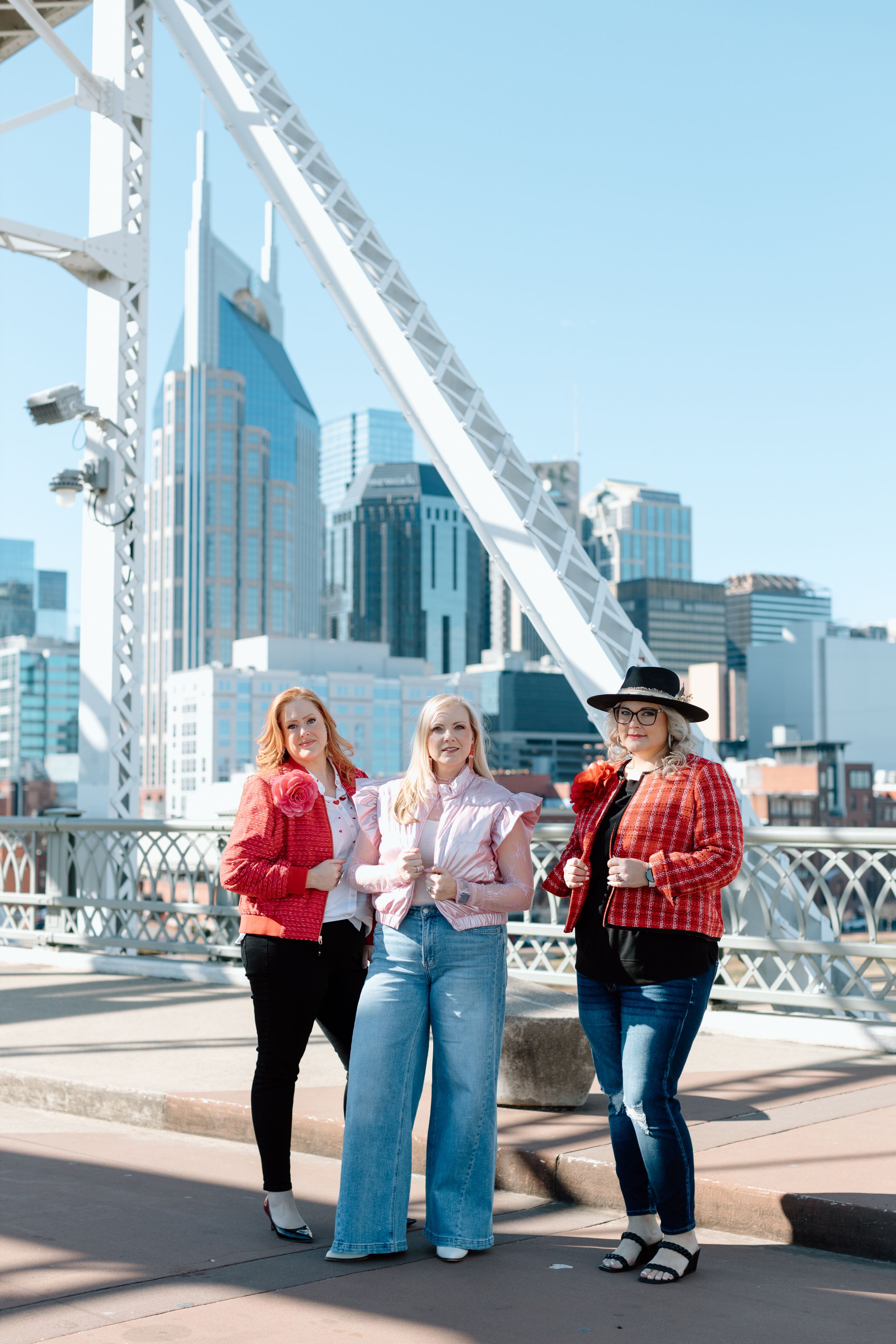 Three people in colorful jackets stroll along a pedestrian bridge with modern city buildings in the background.
