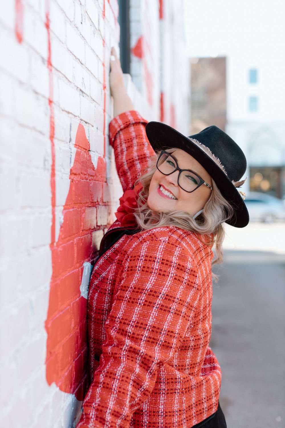 Stylish winter outfit with red plaid jacket and black hat posed against white wall outdoors.