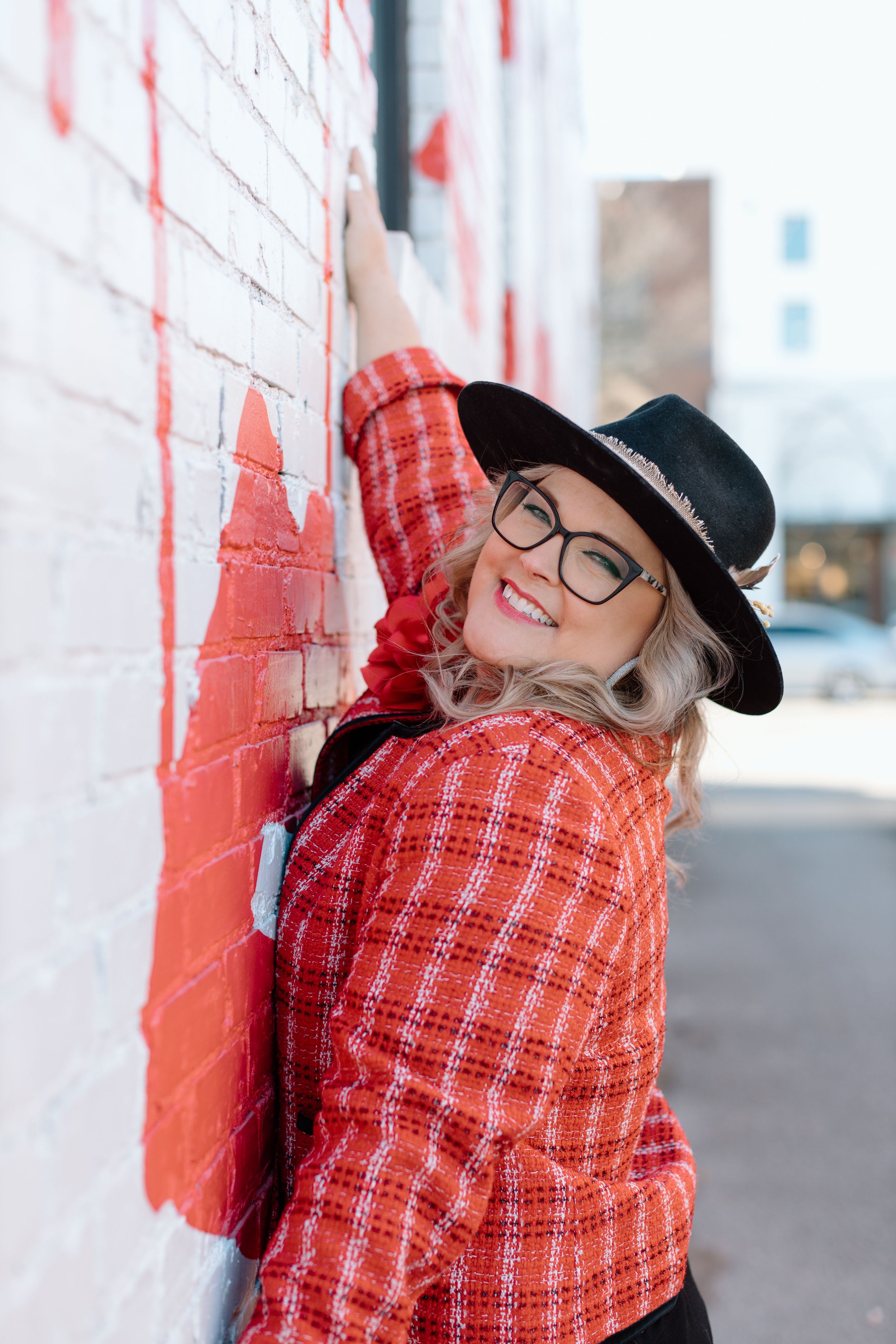 Stylish winter outfit with red plaid jacket and black hat posed against white wall outdoors.