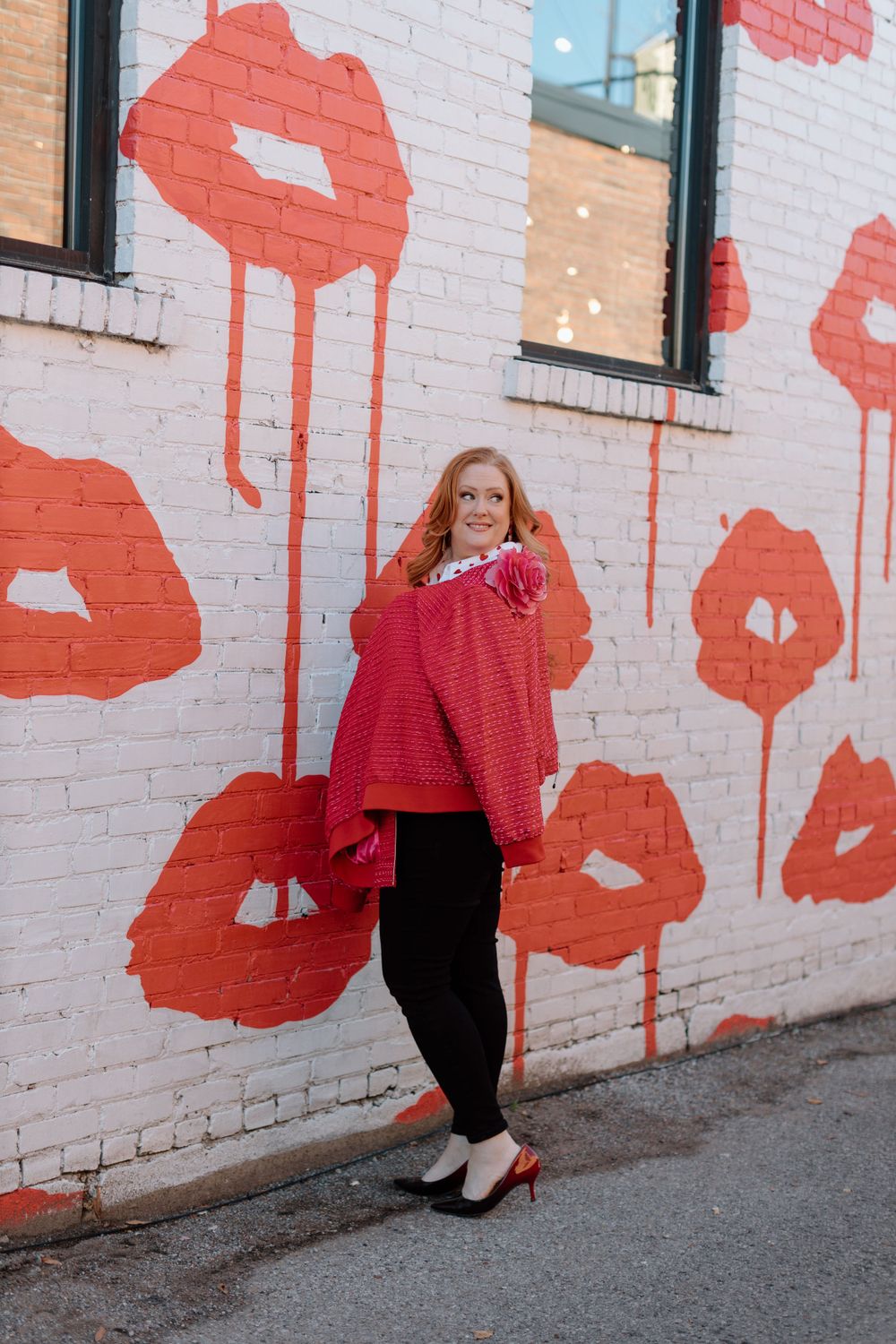 Colorful wall art featuring large red lip prints on white brick creates backdrop for fashion photo shoot outdoors.