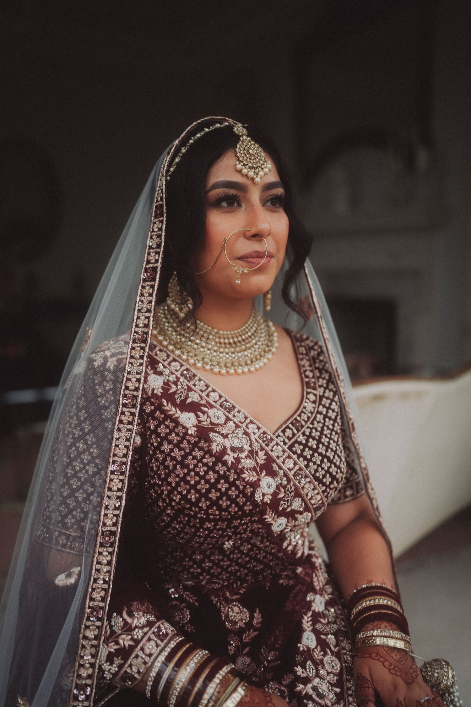 Portrait of bride in burgundy embroidered lehenga with traditional South Asian wedding jewelry.