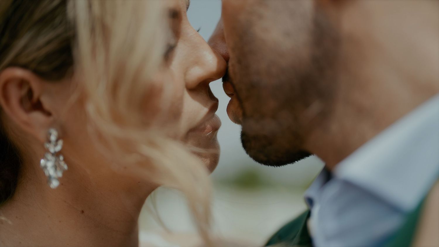 Romantic close-up moment between newlyweds with bride wearing elegant dangling earrings.