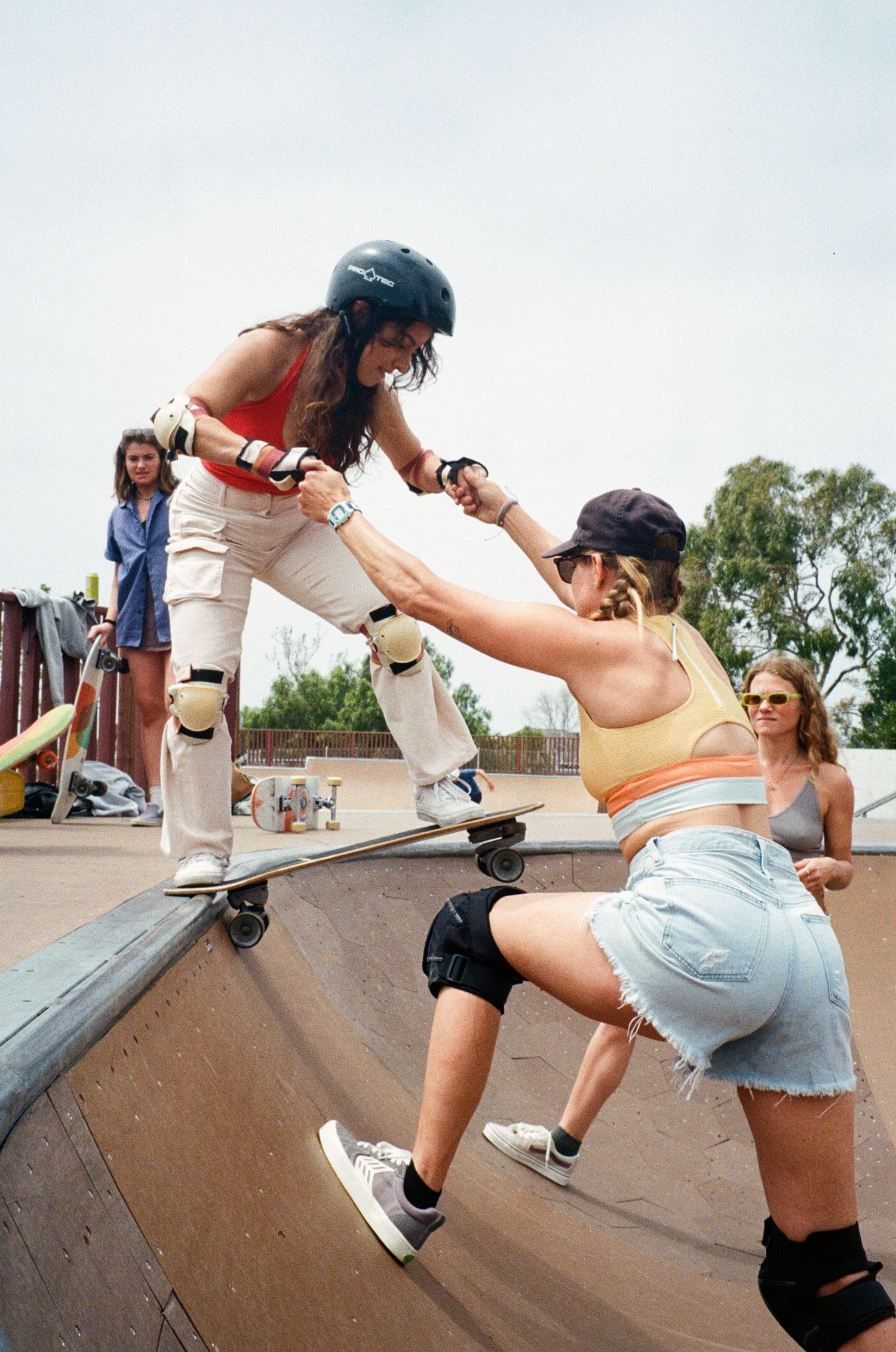 A skater helps another skateboarder learn how to drop into a bowl at the skatepark by holding hands